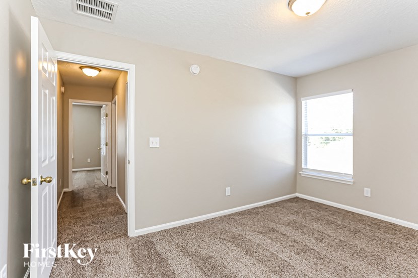 A carpeted room with a window and a door leading to another room.