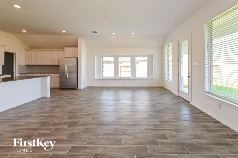 an empty living room with a kitchen in the background