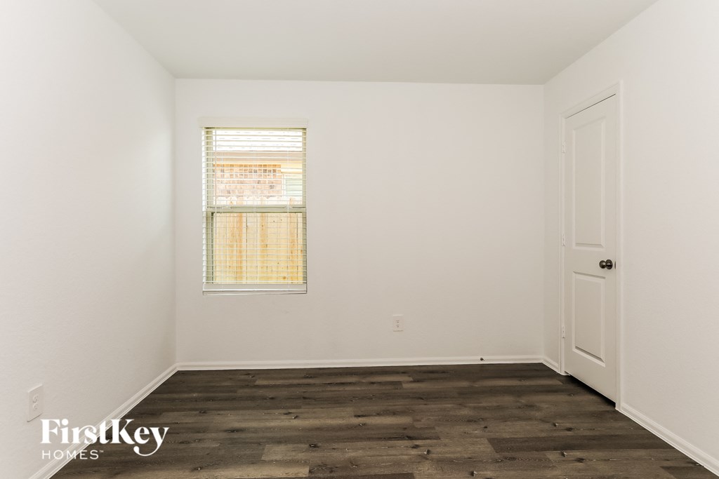 a bedroom with white walls and wood floors and a window