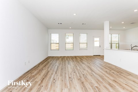 a living room with white walls and wood floors and a kitchen