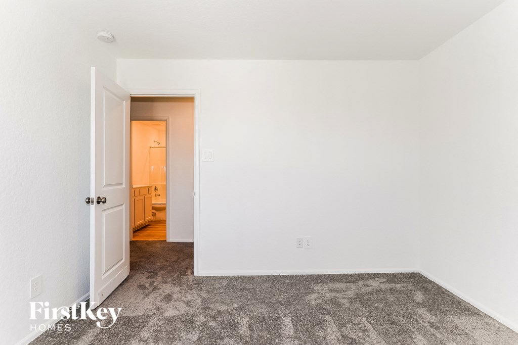 a bedroom with white walls and carpet and a door to a bathroom