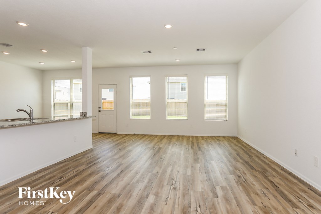 a living room with white walls and wooden floors and a kitchen