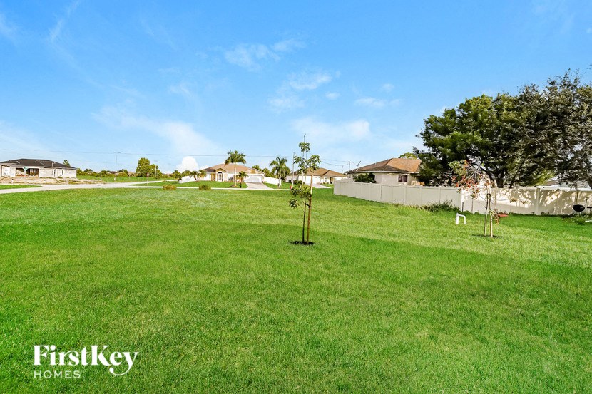 A grassy field with a few trees and a fence in the distance.