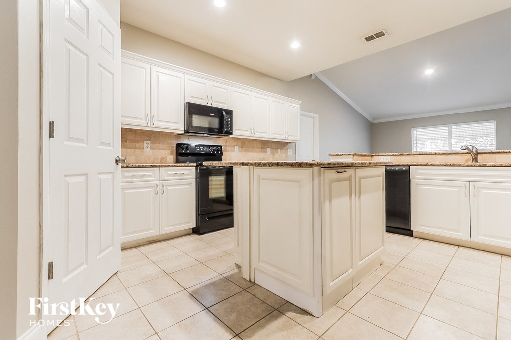 A kitchen with white cabinets and a black microwave.