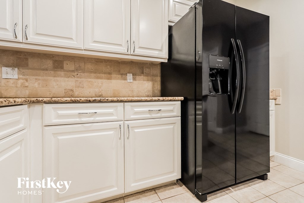 A black refrigerator stands in a kitchen with white cabinets.