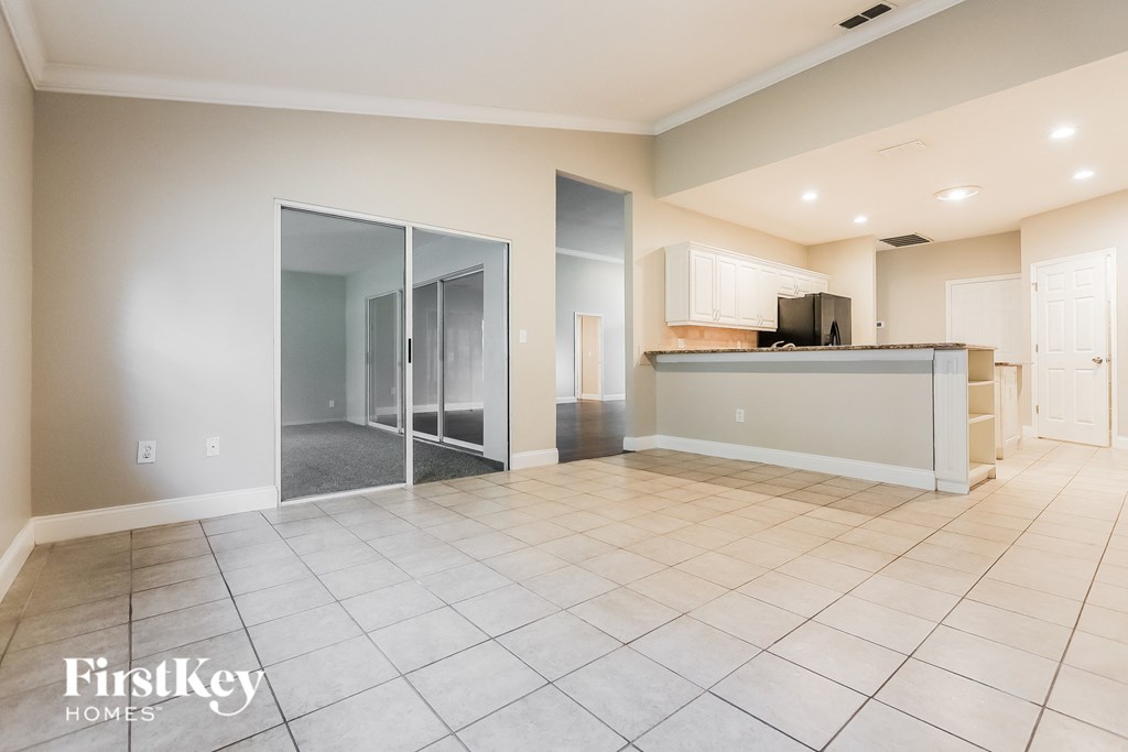 A spacious living room with a kitchen in the background and a tile floor.