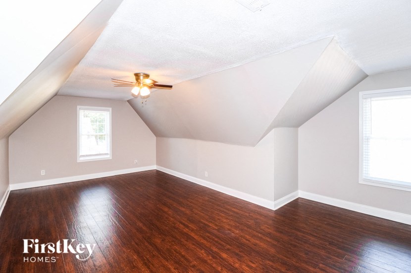 the attic of a home with wood flooring and a ceiling fan