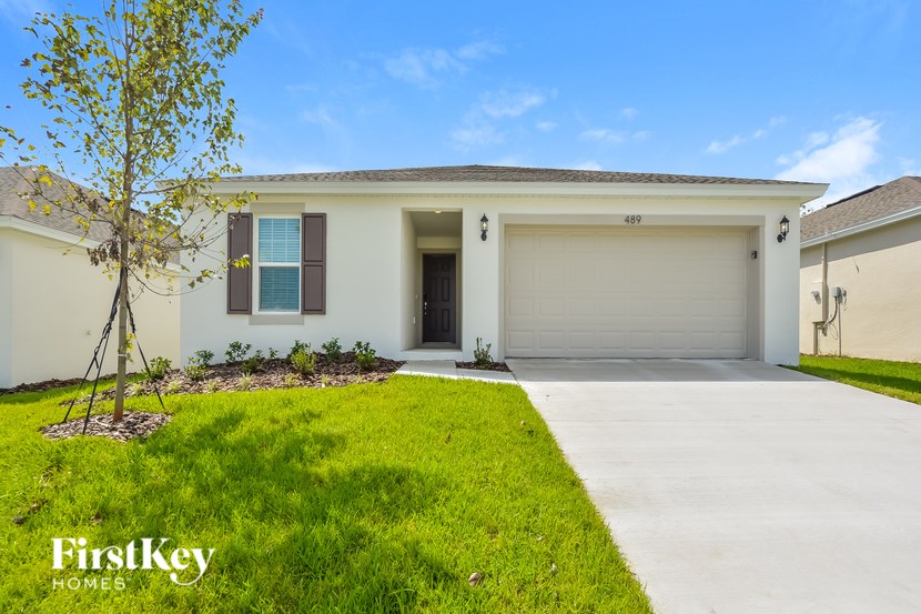 A white house with a garage door and a tree in front of it.