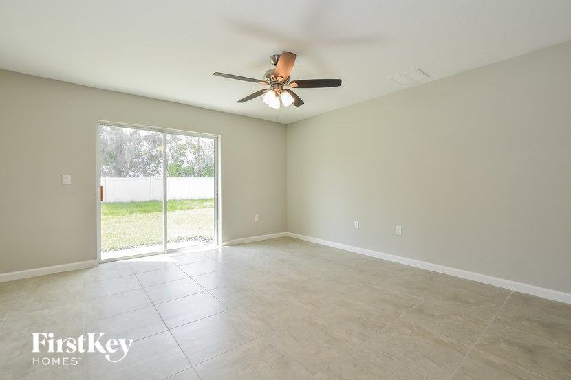 A spacious room with a ceiling fan and sliding glass doors leading to a backyard.