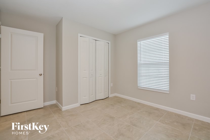 A room with a white door, a white closet, and a window with blinds.