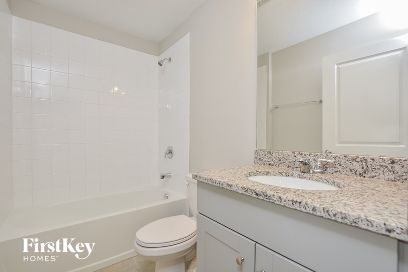 A white bathroom with a marble counter top and a toilet.