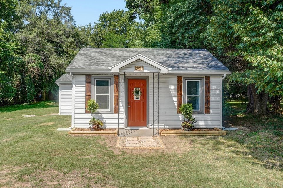 A small house with a red door is surrounded by greenery.