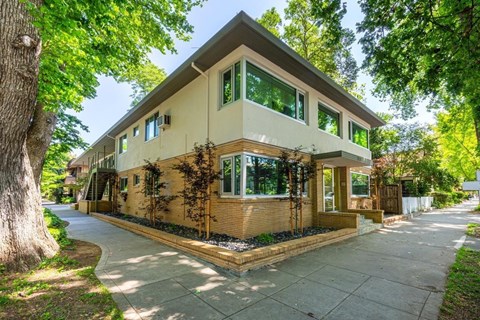 A house with a brown and beige exterior is surrounded by green trees.