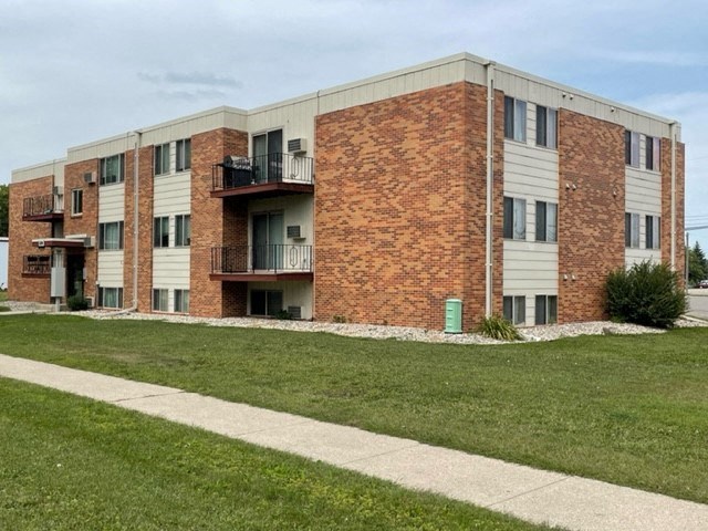 a brick apartment building with grass and a sidewalk