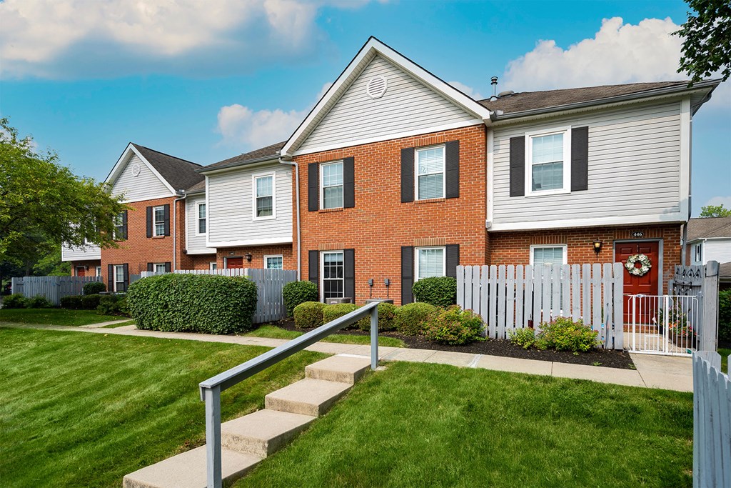the front of a brick house with a white fence and a lawn
