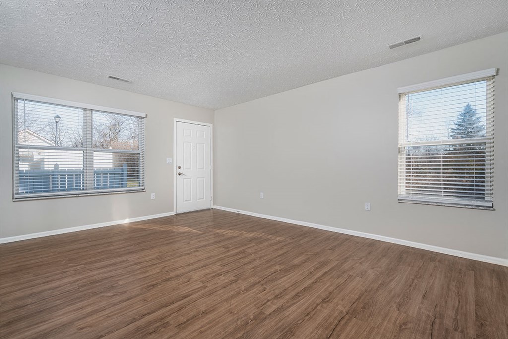 an empty living room with wood flooring and two windows