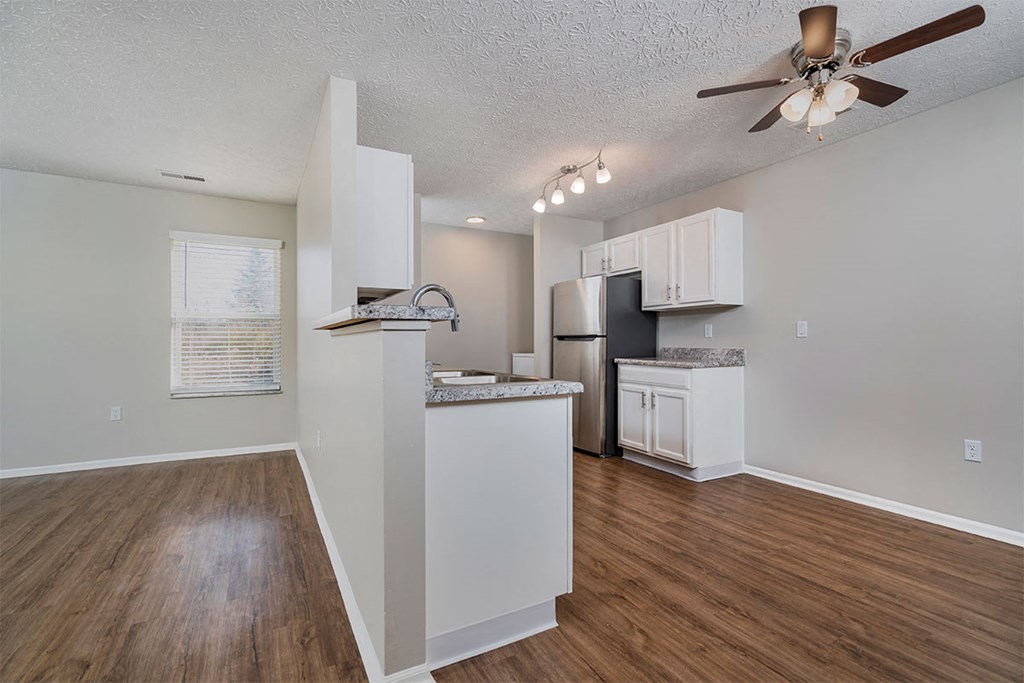 an empty living room with a kitchen and a ceiling fan