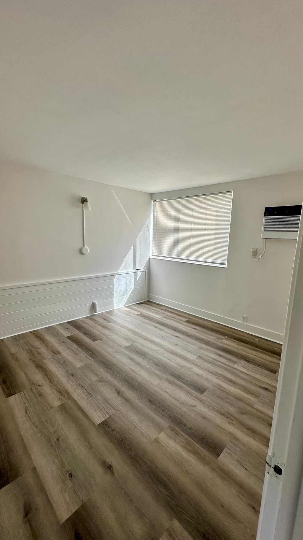 a room with hardwood flooring and white walls and a window