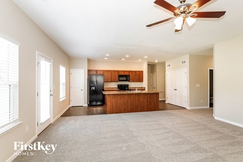 an empty living room with a kitchen and a ceiling fan