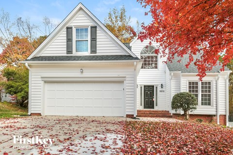A white house with a garage and a tree with red leaves in front.