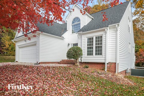 A white house with a red tree in front.