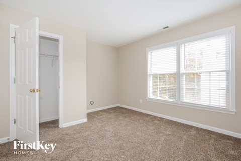 A room with a carpeted floor, a door, and a window with blinds.