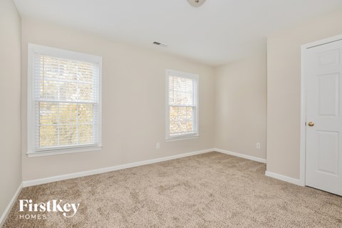 A room with a carpeted floor, a window with blinds, and a door.