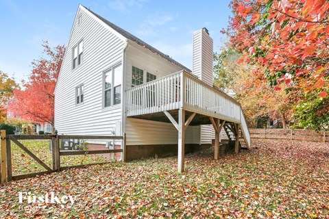 A white house with a balcony is surrounded by fallen leaves.