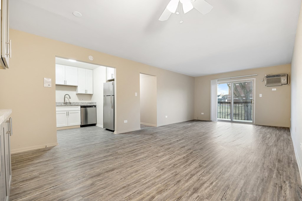 an empty living room with a kitchen and a sliding glass door