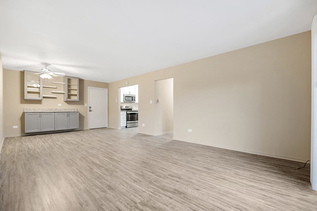 an empty living room and kitchen with a ceiling fan and wood flooring