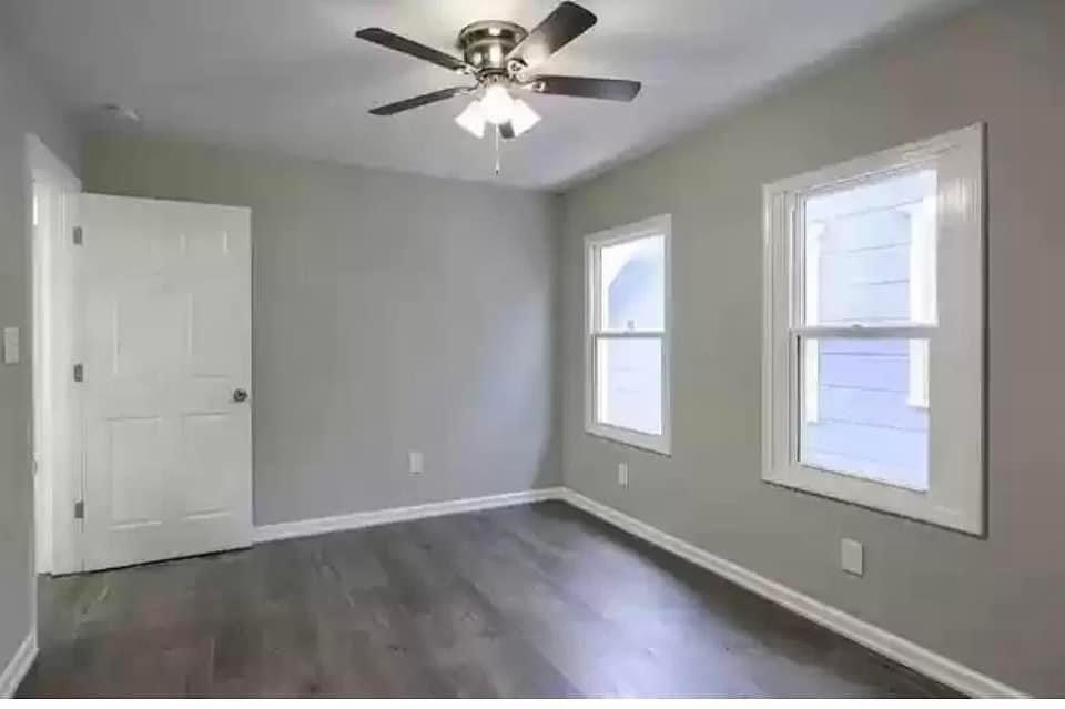 an empty bedroom with a ceiling fan and two windows