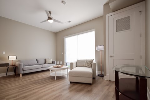 A living room with a grey couch, a white couch, a glass table and a wooden floor.