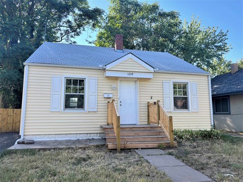 a small yellow house with a wooden porch and a white door