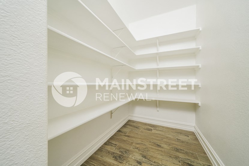 a walk in closet with white shelves and a wood floor