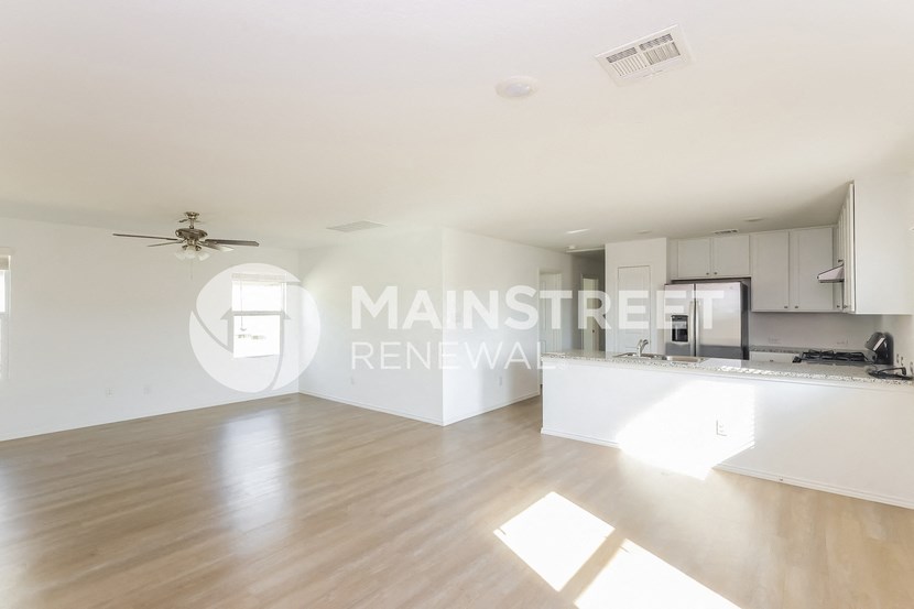 a renovated living room and kitchen with white walls and wood floors