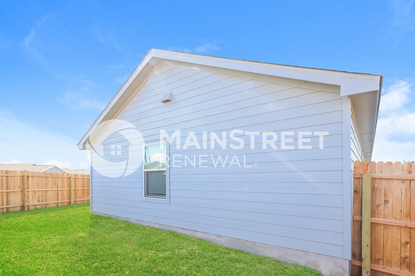 a small white building with a lawn and a wooden fence
