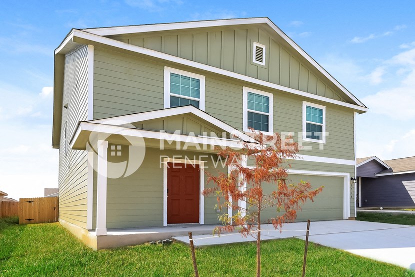 a green house with a garage and a tree in front of it
