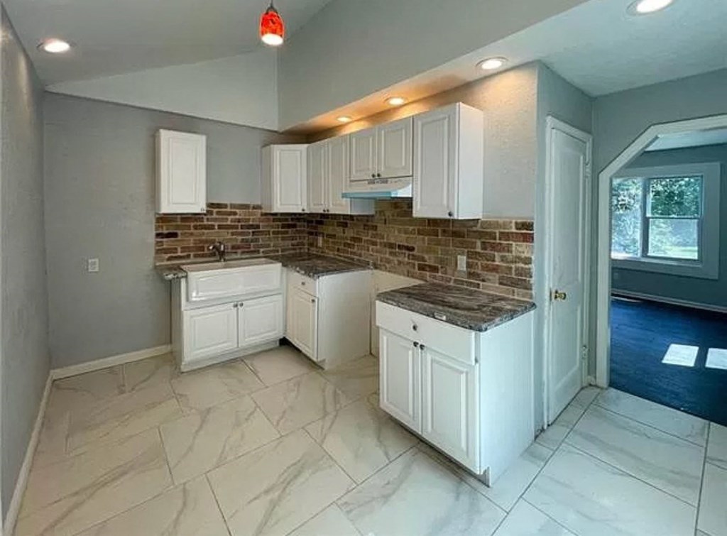 a kitchen with white cabinets and a brick wall