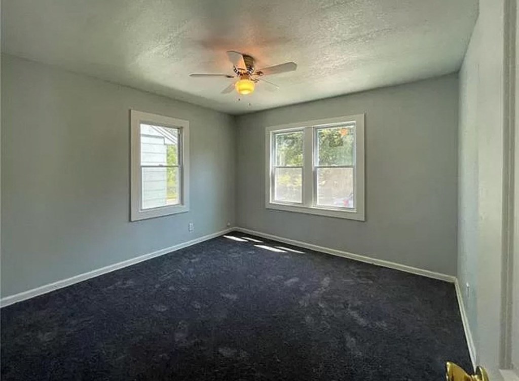 an empty room with a ceiling fan and two windows