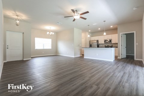 an empty living room with a ceiling fan and a kitchen