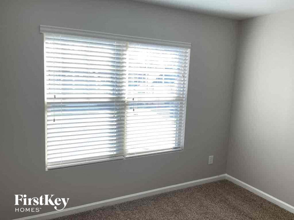 A room with a carpeted floor and a window covered with white blinds.
