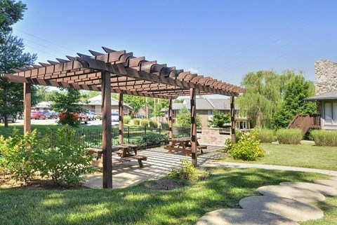 A wooden pergola with a bench underneath it is situated in a grassy area.