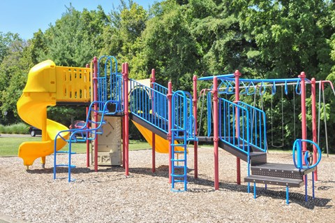 A playground with a yellow slide, blue and red climbing structures, and a grey platform.