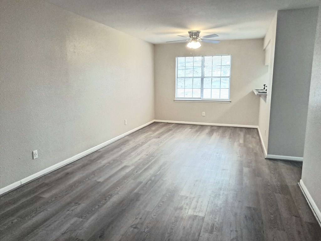 an empty living room with wood floors and a ceiling fan
