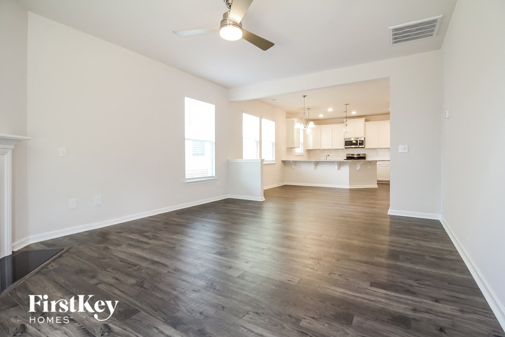 an empty living room and kitchen with wood flooring and a ceiling fan