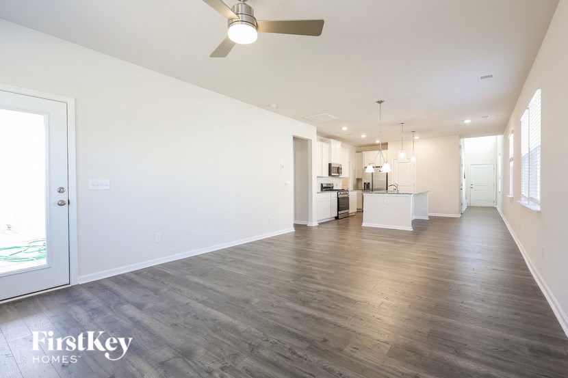 A spacious room with a kitchen area in the background and a ceiling fan above.
