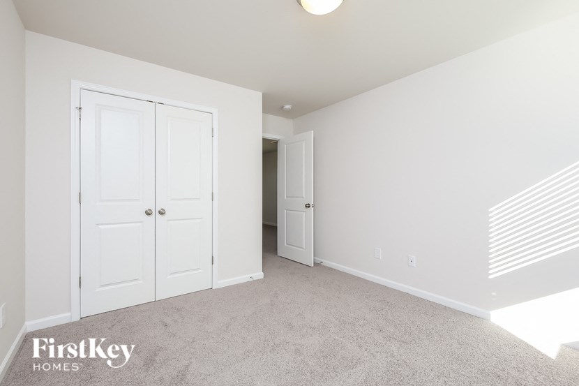 A white bedroom with a carpet floor and a FirstKey Homes logo.