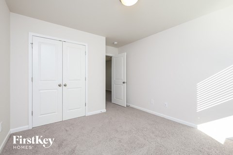 A white bedroom with a carpet floor and a FirstKey Homes logo.