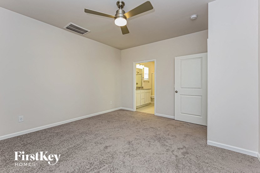 an empty living room with a ceiling fan and a door to a bathroom