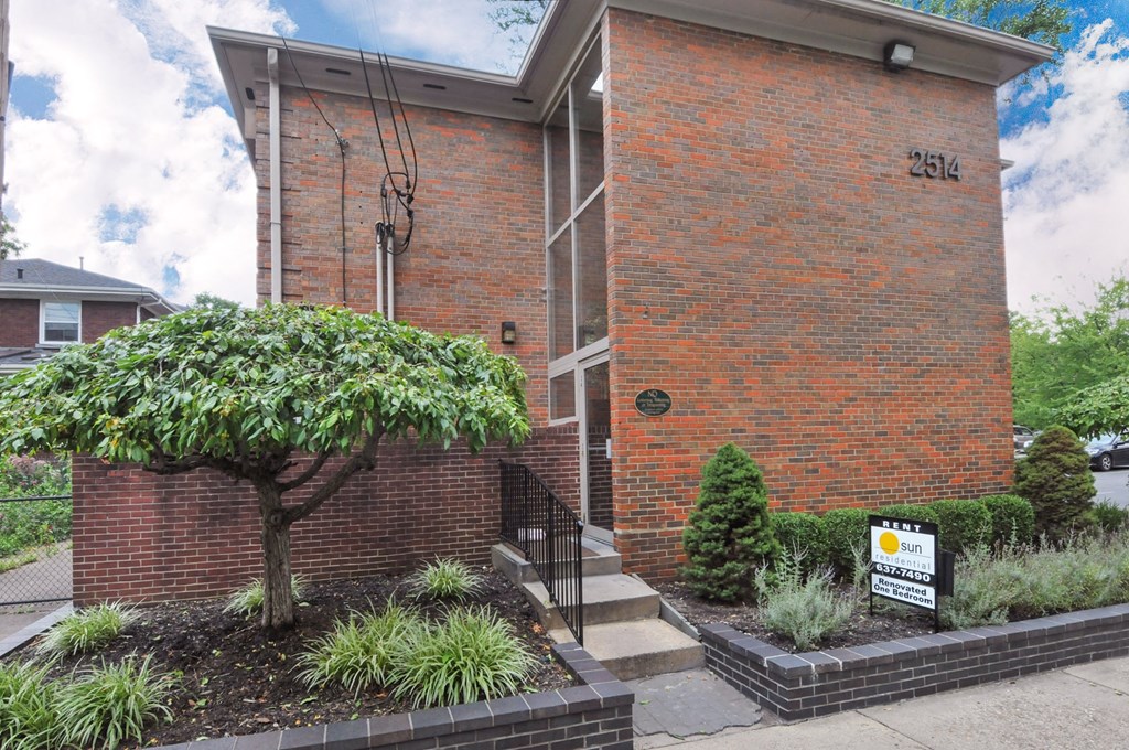 A red brick building with a sign that says "For Sale" in front of it.